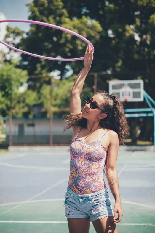 a woman standing on top of a tennis court holding a hula hoop, pexels contest winner, wearing : tanktop, isabela moner, urban playground, curly haired