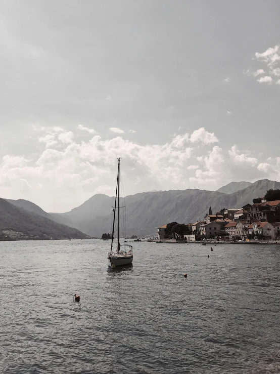 a black and white photo of a boat in the water, by Emma Andijewska, pexels contest winner, mountains and a huge old city, boka, in muted colours, sunny day time