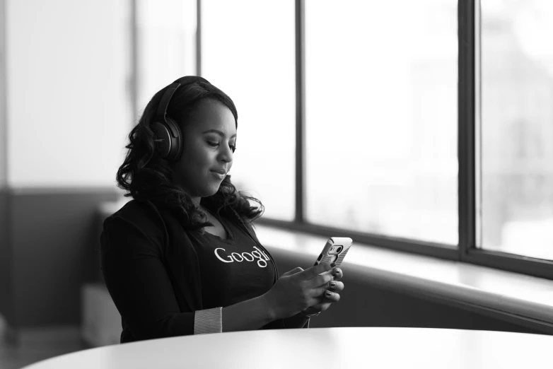 a woman sitting at a table looking at her cell phone, a black and white photo, pexels, wearing headset, african female android, google, people at work