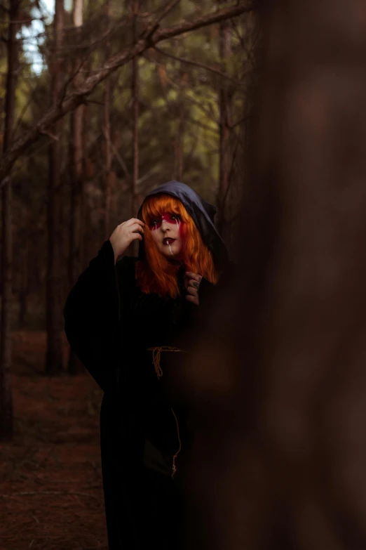 a woman with red hair standing in a forest, a photo, pexels contest winner, renaissance, wearing black wizard robes, scaring, cloak covering face, slightly pixelated