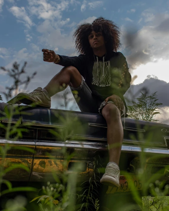 a woman sitting on top of a car in a field, an album cover, trending on unsplash, graffiti, east african man with curly hair, intimidating pose, sneaker photo, lgbtq