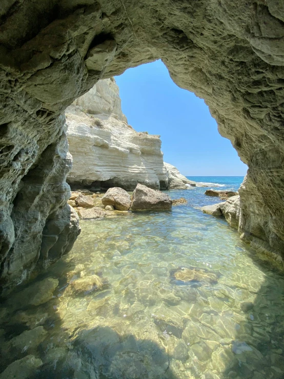 a cave in the middle of a body of water, near the beach, aphrodite, youtube thumbnail, national geograph