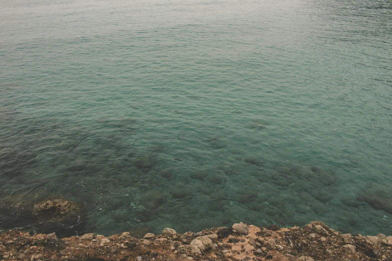 a large body of water next to a rocky shore, a picture, inspired by Elsa Bleda, unsplash, happening, cyprus, low quality photo, alessio albi, teal