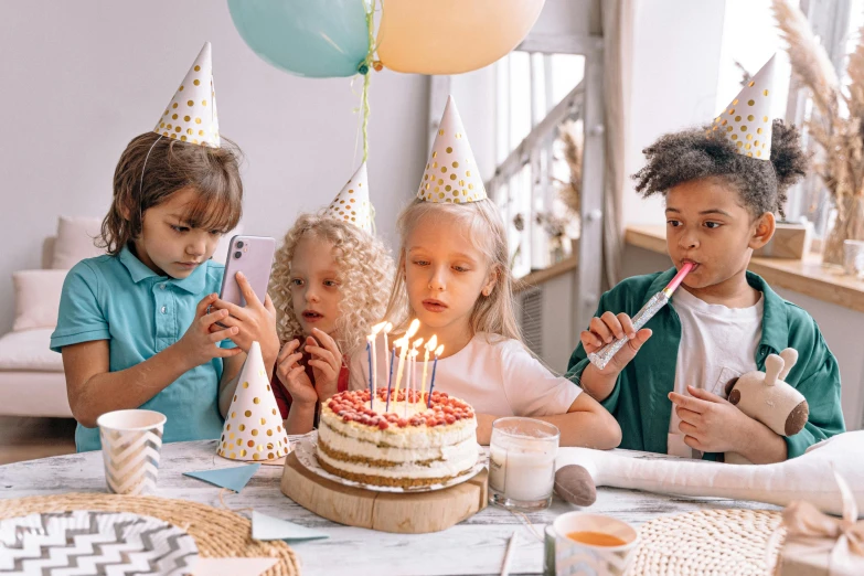 a group of children sitting at a table with a birthday cake, by Elaine Hamilton, pexels, fan favorite, white candles, table with microphones, [ cinematic