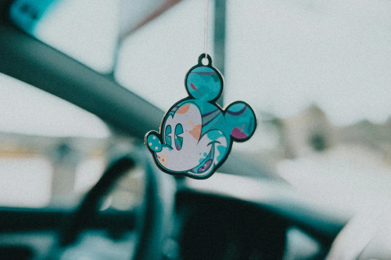 a mickey mouse hanging from the dashboard of a car, a cartoon, pexels contest winner, graffiti, teal paper, dreamy hazy, holographic plastic, high quality product image”