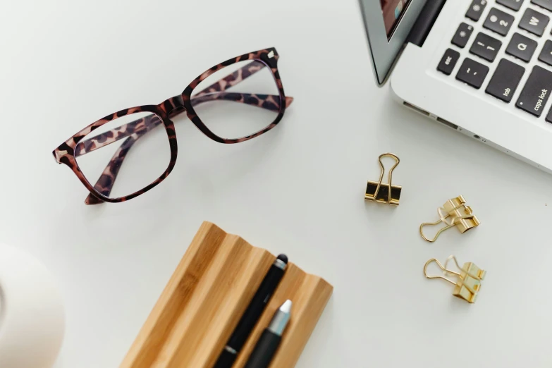 a laptop computer sitting on top of a white desk, glasses frames, curated collections, a wooden, middle close up