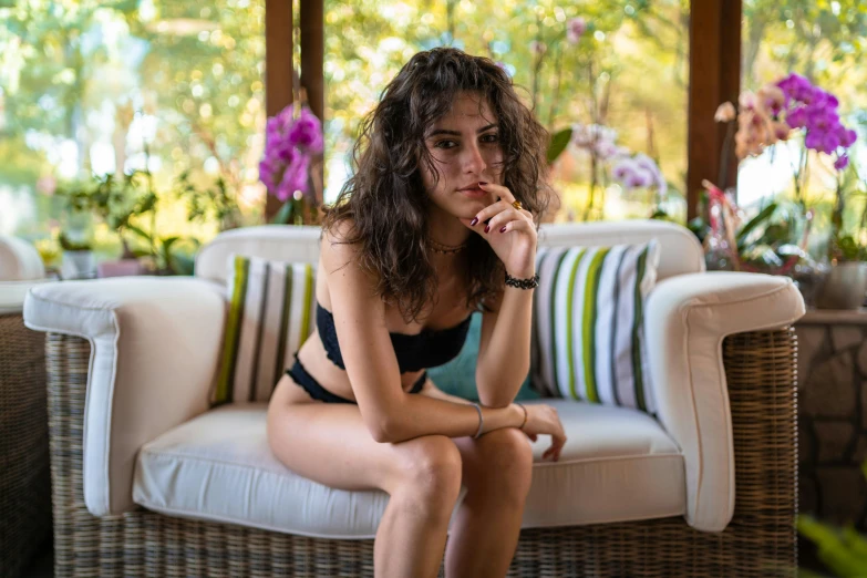 a woman in a bikini sitting on a couch, a portrait, pexels contest winner, teenager hangout spot, profile image, middle eastern skin, lush surroundings