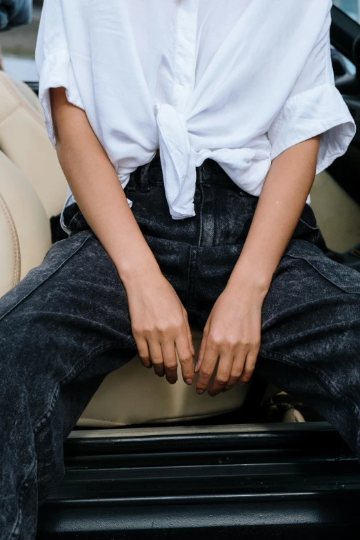 a woman sitting in the driver's seat of a car, by Nina Hamnett, trending on pexels, happening, worn pants, androgyny, texture detail, in a rock chair