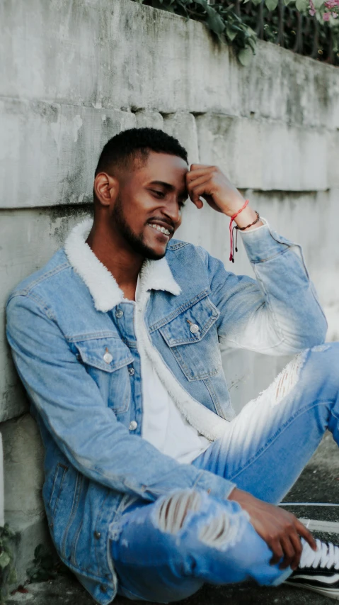 a man sitting on the ground next to a wall, an album cover, pexels contest winner, mkbhd, dramatic smile pose, wearing a jeans jackets, profile image