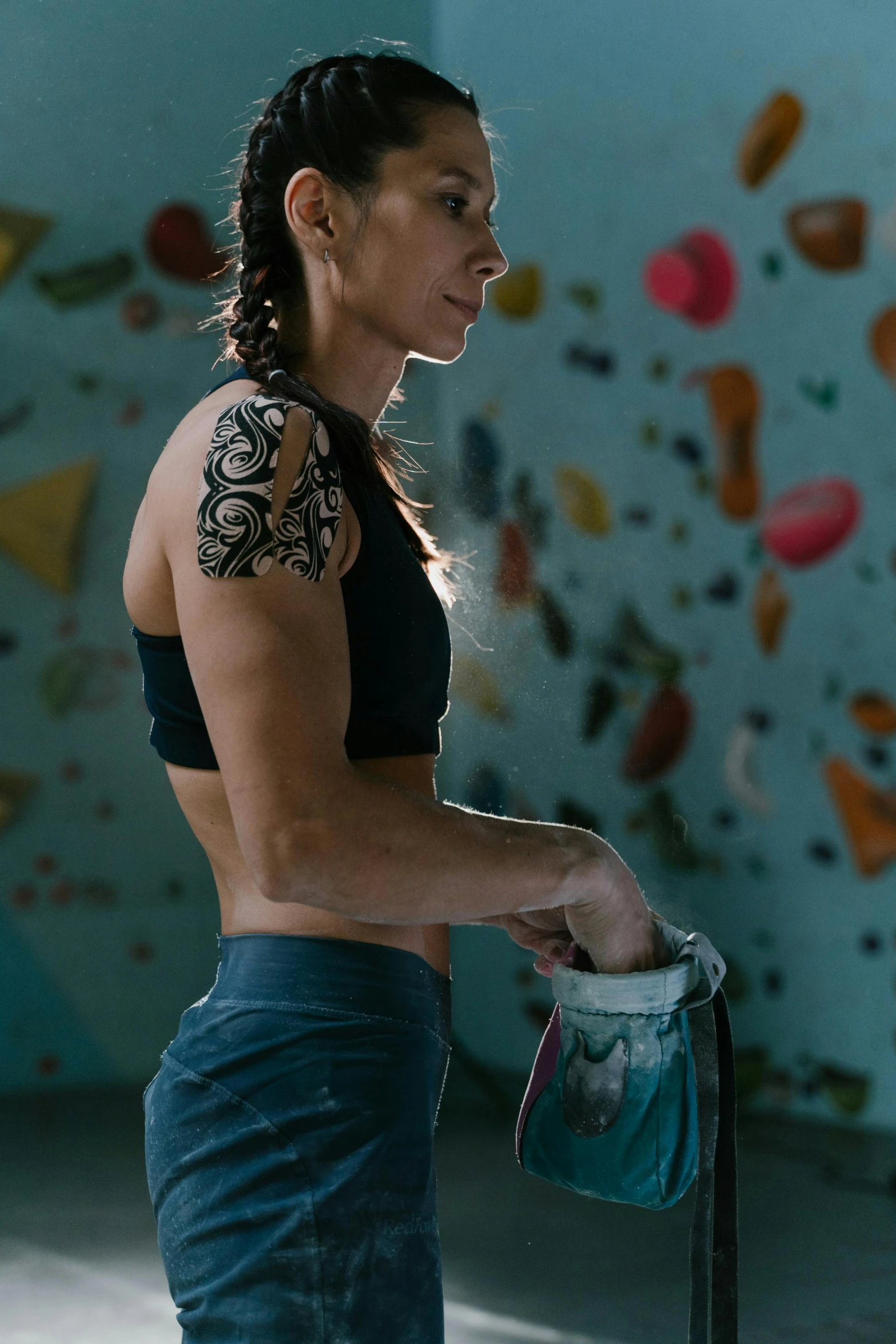 a woman standing in front of a rock climbing wall, a tattoo, profile image