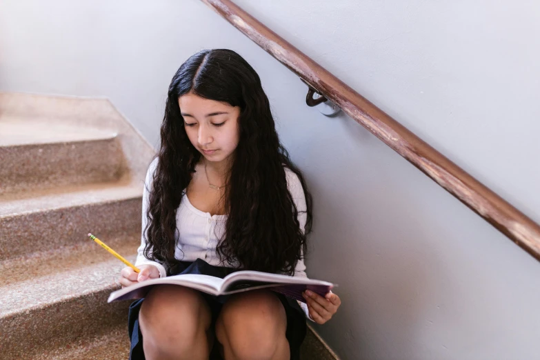 a girl sitting on the stairs reading a book, by Meredith Dillman, pexels contest winner, standing in class, an olive skinned, te pae, aged 13