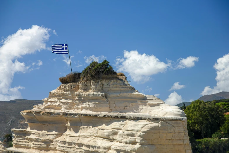 a large rock with a flag on top of it, inspired by Exekias, pexels contest winner, neoclassicism, square, national geograph, geological strata, the greek goddess aphrotite