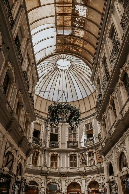 the inside of a building with a glass roof, inspired by Luis Paret y Alcazar, baroque, round buildings in background, neoclassicism style, head straight down, things hanging from ceiling