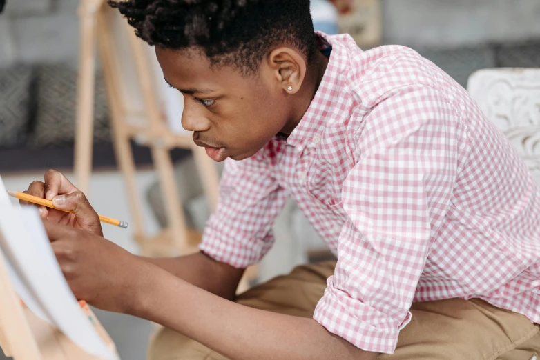 a boy that is sitting down with a pencil in his hand, pexels contest winner, black teenage boy, looking across the shoulder, academic painting, teaching