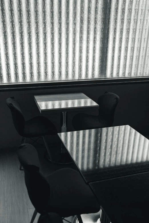 a black and white photo of a desk and chair, by Yasushi Sugiyama, postminimalism, cafe tables, shiny reflective surfaces, soft light through blinds, todd hido photography