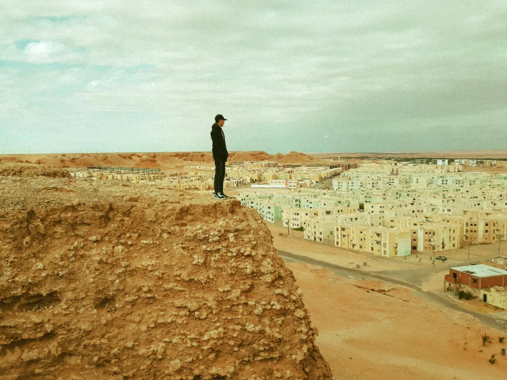 a man standing on top of a dirt hill, by Nathalie Rattner, pexels contest winner, surrealism, arab man, cliffside town, lo-fi, highly complex