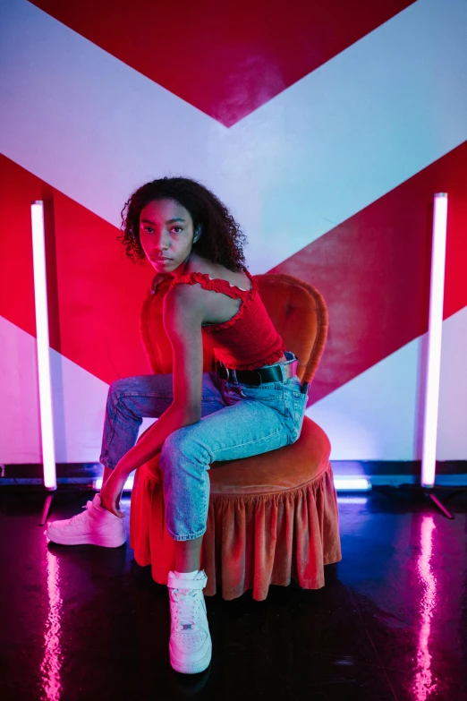 a woman sitting on a chair in front of a red and white wall, ashteroth, flashy red lights, posing for a picture, bounce lighting