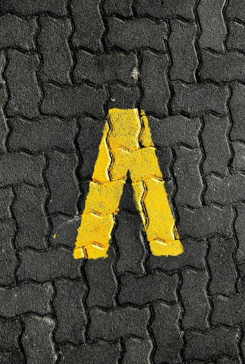 a street sign with the letter a painted on it, a mosaic, by Adam Marczyński, unsplash, yellow charcoal, tyre mark, non-binary, avatar image