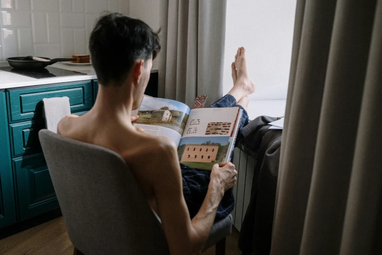 a man sitting in a chair reading a book, a picture, by Emma Andijewska, pexels contest winner, wearing nothing, non binary model, looking outside, anatomy book