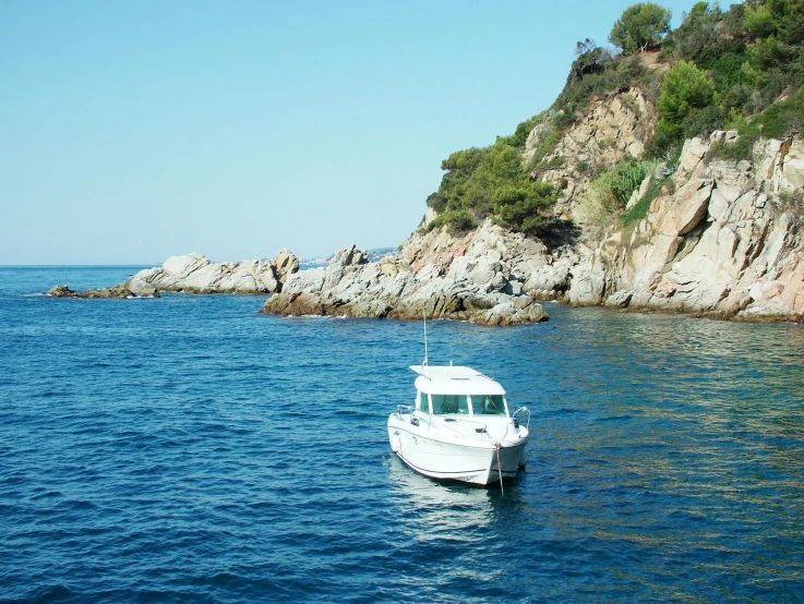 a white boat floating on top of a body of water, les nabis, rocky coast, quintessa, in barcelona, picton blue