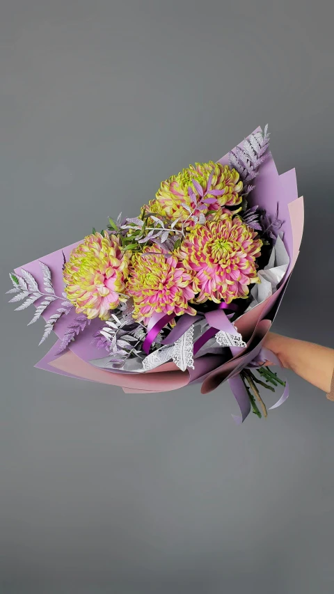 a person holding a bunch of flowers in their hand, purple neon colours, on grey background, paper chrysanthemums, vibrant foliage