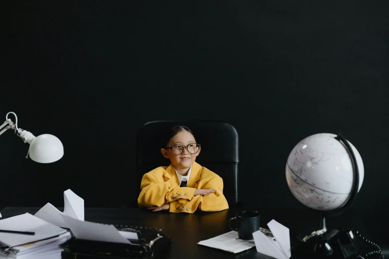 a little boy sitting at a desk in front of a globe, pexels contest winner, woman in black business suit, yellow and black color scheme, pilot girl, wearing jacket and skirt