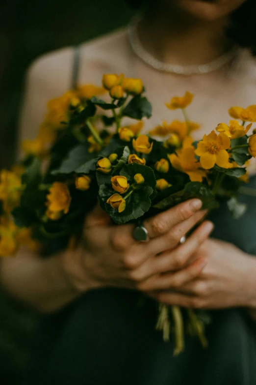 a woman holding a bunch of yellow flowers, inspired by Elsa Bleda, unsplash, wearing gilded ribes, somber mood, lush flora, no watermark