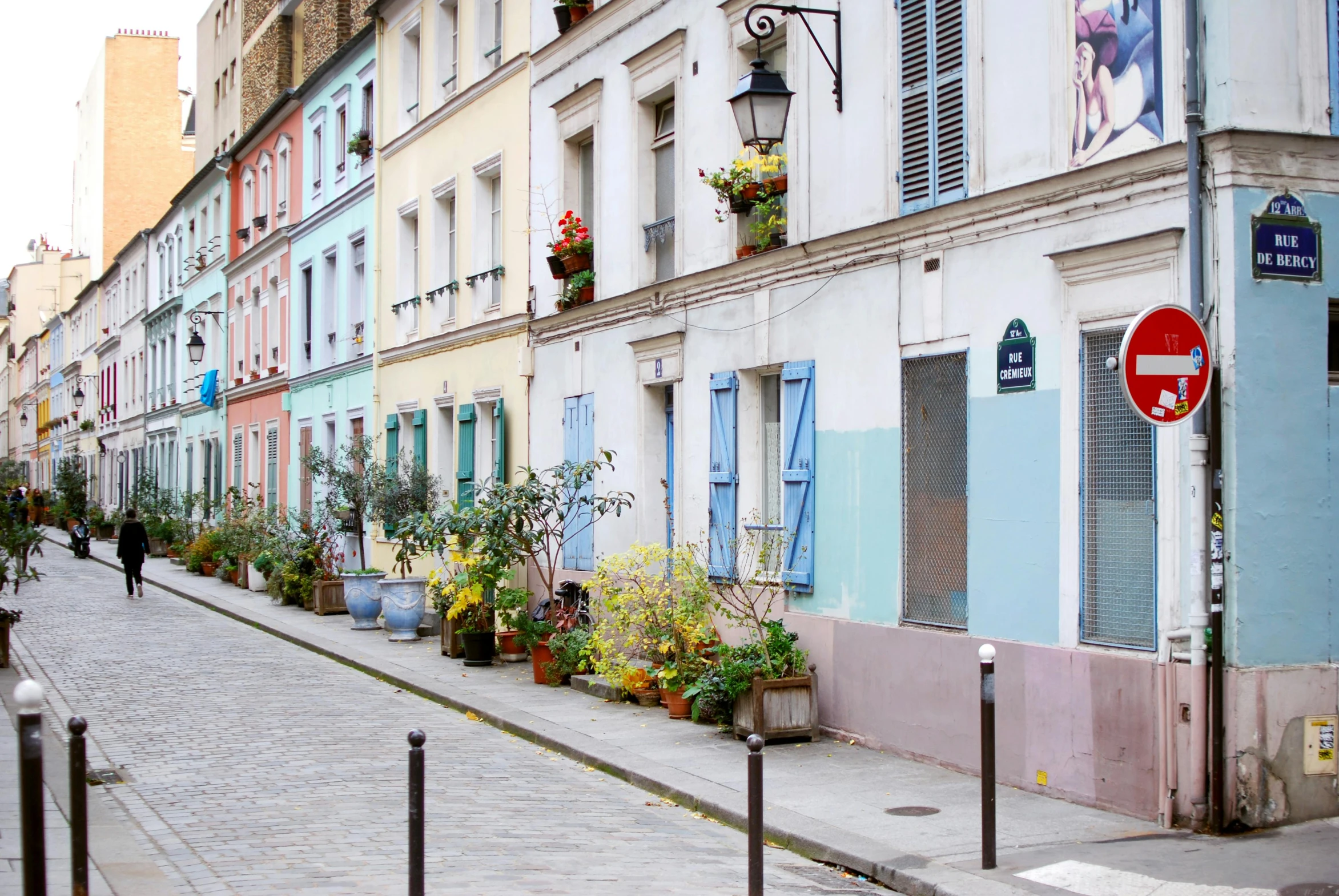 a red stop sign sitting on the side of a road, a photo, inspired by Maurice Utrillo, trending on unsplash, paris school, pink and blue palette, plants on pots and on the walls, colorful houses, alley