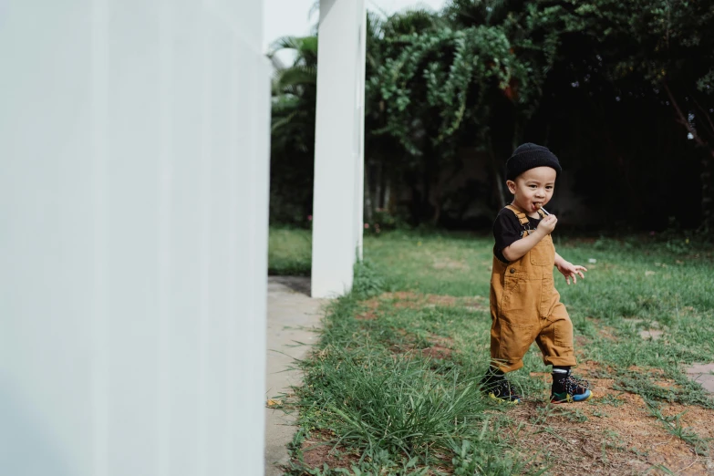 a little boy that is standing in the grass, pexels contest winner, overalls, outlive streetwear collection, black and brown colors, thawan duchanee