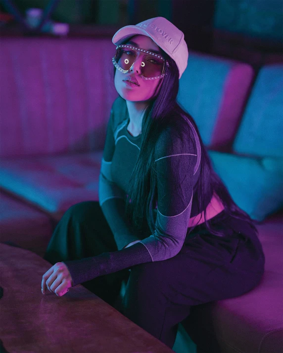 a woman sitting on a couch in a living room, an album cover, inspired by Elsa Bleda, trending on pexels, visual art, with neon visor, asian women, wearing goggles, dark moody purple lighting