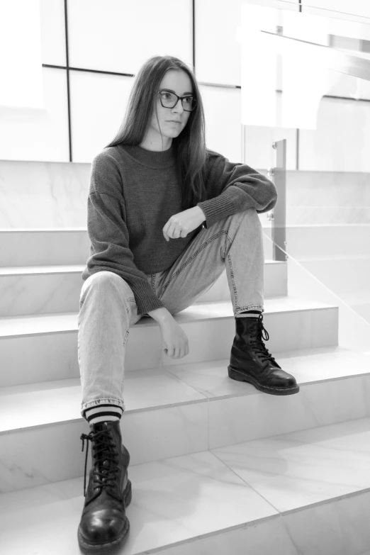 a black and white photo of a woman sitting on steps, inspired by Anita Malfatti, tumblr, hyperrealism, with square glasses, jeans and boots, standing in corner of room, androgynous person