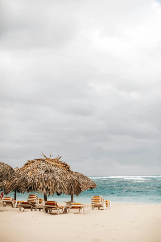 a couple of umbrellas sitting on top of a sandy beach, thatched roof, aruba, overcast skies, square