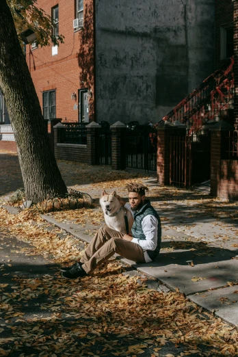 a man sitting on the sidewalk with a dog, a photo, by Julia Pishtar, pexels contest winner, in fall, cool pose, chicago, in the yard