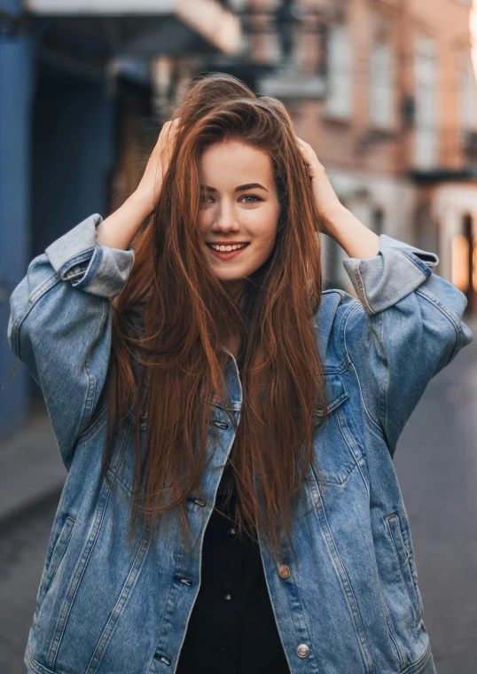 a woman standing on a street with her hands on her head, pexels contest winner, renaissance, wearing a jeans jackets, long wavy auburn hair, better known as amouranth, happily smiling at the camera