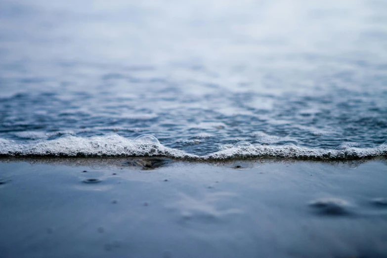 a body of water sitting on top of a sandy beach, a picture, unsplash, close - up photograph, blue and grey, wave, thin dof