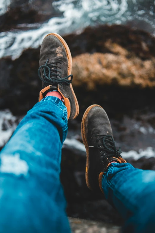 a person sitting on top of a rock next to the ocean, trending on pexels, renaissance, jeans and boots, gum rubber outsole, full frame image, portrait of tall