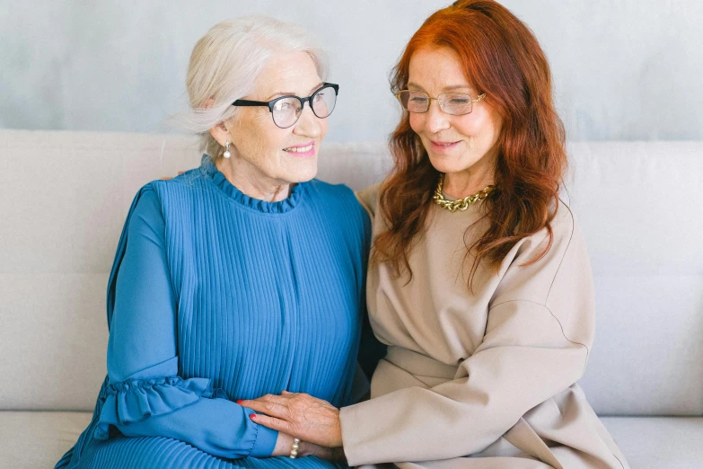 two women sitting next to each other on a couch, a portrait, by Emma Andijewska, trending on pexels, wearing square glasses, elderly, woman with red hair, silver haired