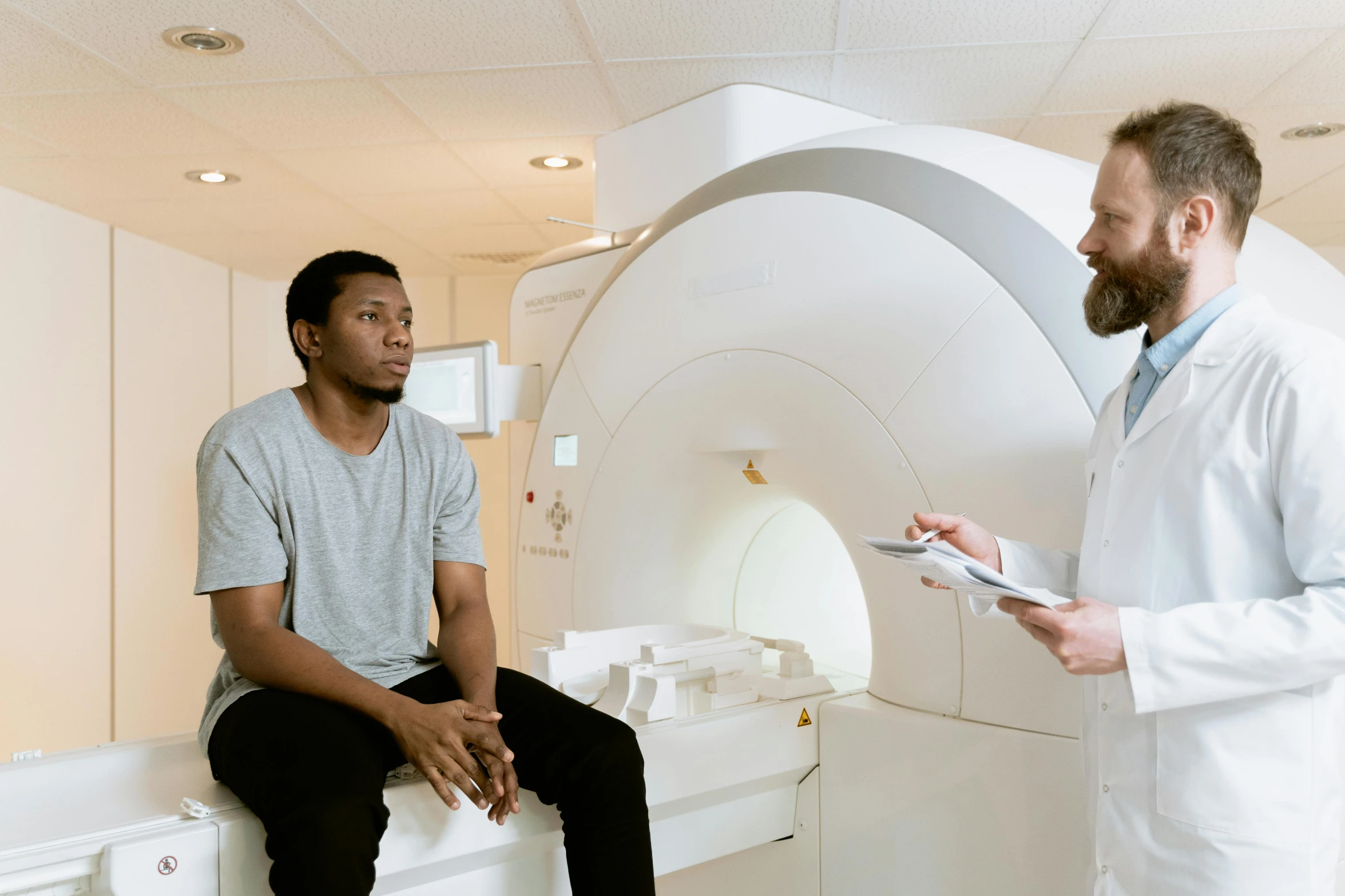 a couple of men standing next to each other in a room, mri, sitting down, diverse, brown