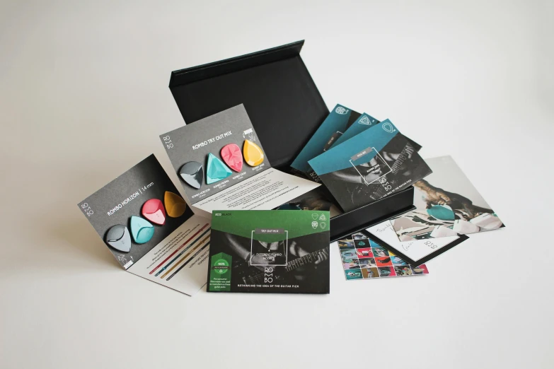 a pile of brochures sitting on top of a table, a pastel, inspired by Eden Box, black and teal paper, various posed, kit, innovation