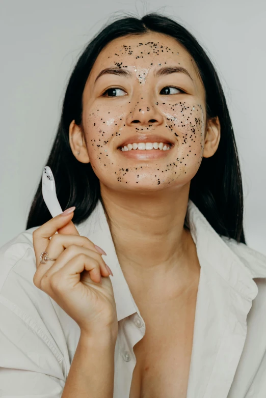 a woman holding a toothbrush in front of her face, by Julia Pishtar, happening, white with black spots, south east asian with round face, mole on cheek, glitter accents on figure