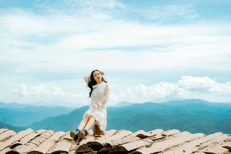 a woman sitting on top of a roof with mountains in the background, inspired by Ma Yuanyu, pexels contest winner, romanticism, ao dai, happy girl, avatar image, wearing a white dress