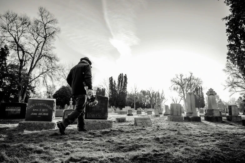 a black and white photo of a man walking in a cemetery, a black and white photo, pexels, happening, man with scythe, morning golden hour, professional work, graveside