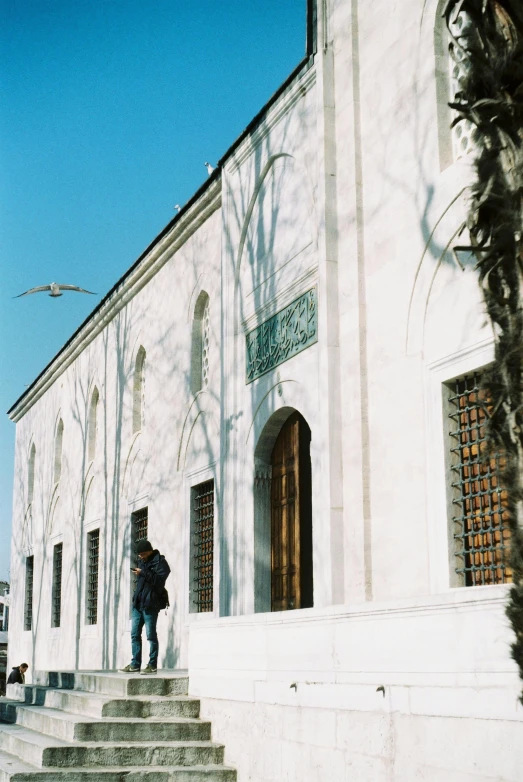 a man standing on the steps of a building, a marble sculpture, inspired by Osman Hamdi Bey, trending on pexels, arabesque, white building, 1990s photograph, winter, old library