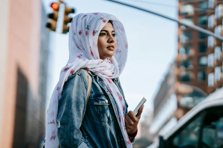 a woman in a hijab is looking at her cell phone, trending on pexels, in the middle of new york, white scarf, proud looking away, swedish