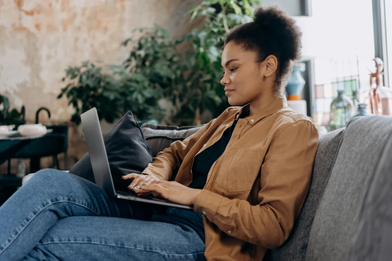 a woman sitting on a couch using a laptop, a portrait, trending on pexels, from the side, brown, black female, developers