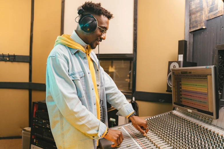 a man standing in front of a mixing desk, trending on pexels, wearing a yellow hoodie, real sousaphones, student, ad image