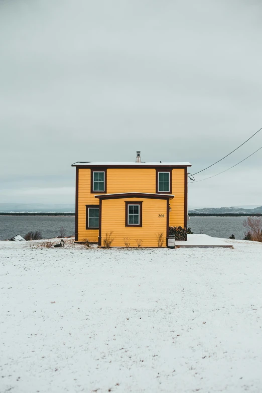 a yellow house sitting on top of a snow covered field, inspired by Wes Anderson, pexels contest winner, renaissance, coastal, grey, quebec, 8k photo