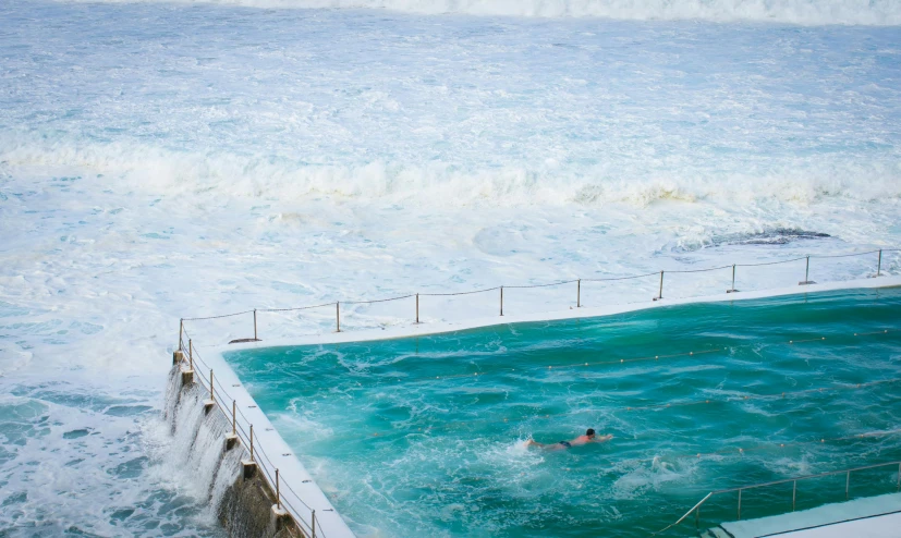 a man swimming in a pool next to the ocean, by Peter Churcher, pexels contest winner, wall of water either side, bondi beach in the background, an eerie whirlpool, farming