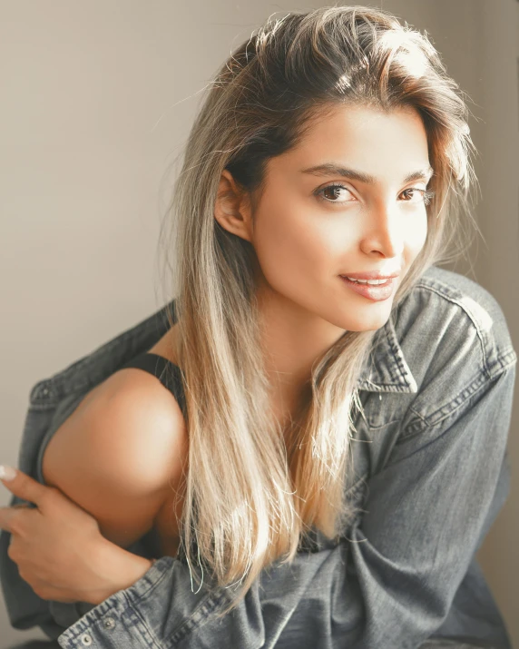 a woman sitting on top of a bed next to a window, trending on unsplash, alone gorgeous latin woman, ash blond greyish hair, lovingly looking at camera, wearing a jeans jackets