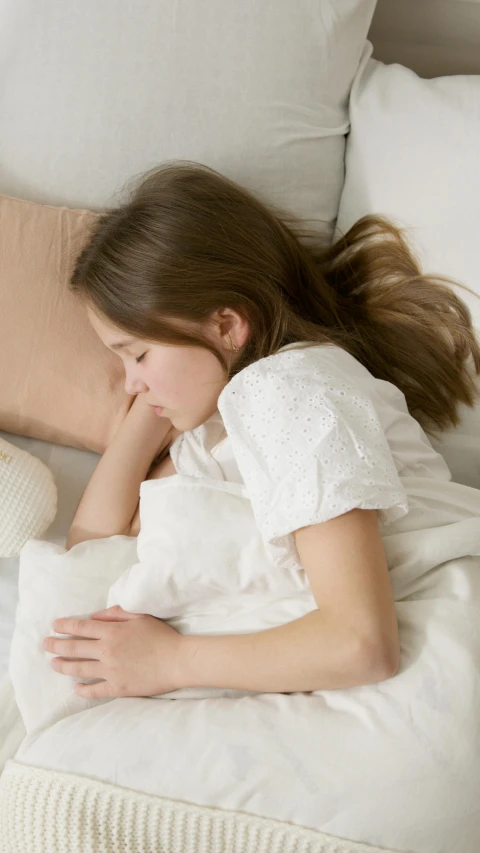 a woman laying on top of a bed next to a teddy bear, pexels, cream and white color scheme, portrait of depressed teen, 15081959 21121991 01012000 4k, light beige pillows